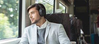  A male on a train wearing the Sony WH-1000XM3 Headphones looking out of the window 